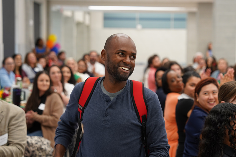 man smiling with room full of people behind him