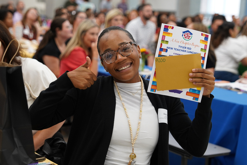 woman giving a thumbs up while holding a certificate with a room full of people behind her