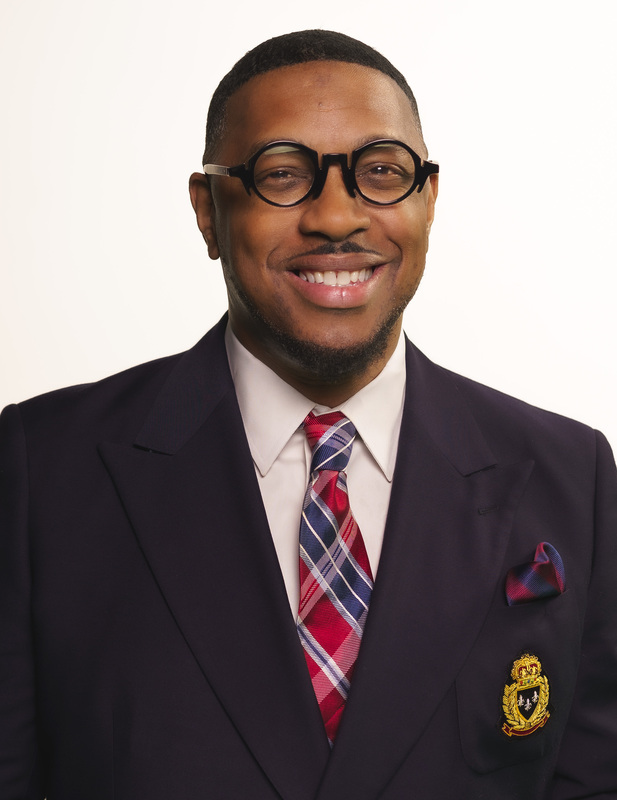 African American man with round black glasses wearing a black suit and tie