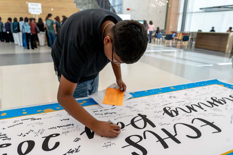 teen boy signs banner showing he plans to attend Early College High School