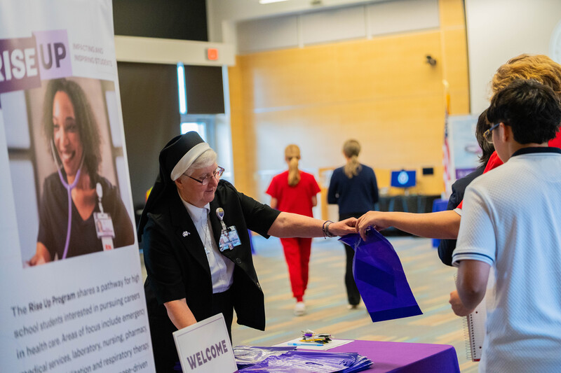 Nun handing purple bags to teens as they enter a room
