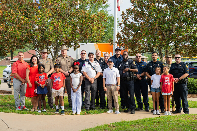 group of men, women, and children standing together in front of flag pole