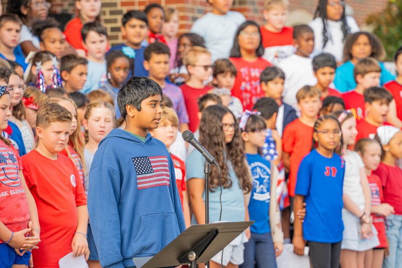 teen boy talking into microphone with elementary age kids standing behind him