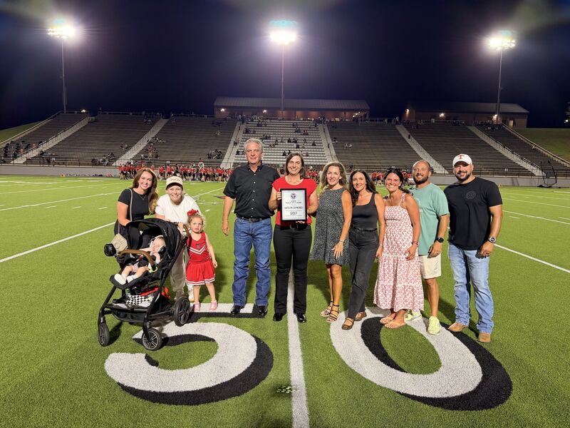 Katelyn Sepmoree holding certificate with her family on the 50 yard line of a football field