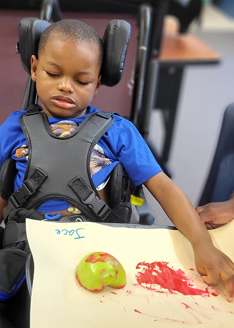 young boy in wheelchair using an apple to paint on paper
