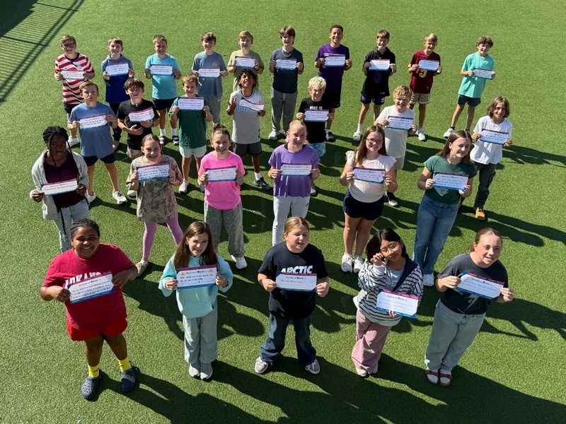 group of young kids standing in middle of green yard holding up signs