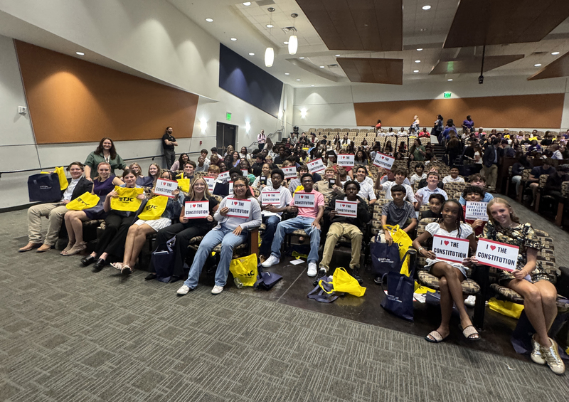 group of high school kids sitting in auditorium holding signs