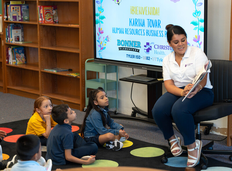 woman sitting in chair reading story to students sitting on floor
