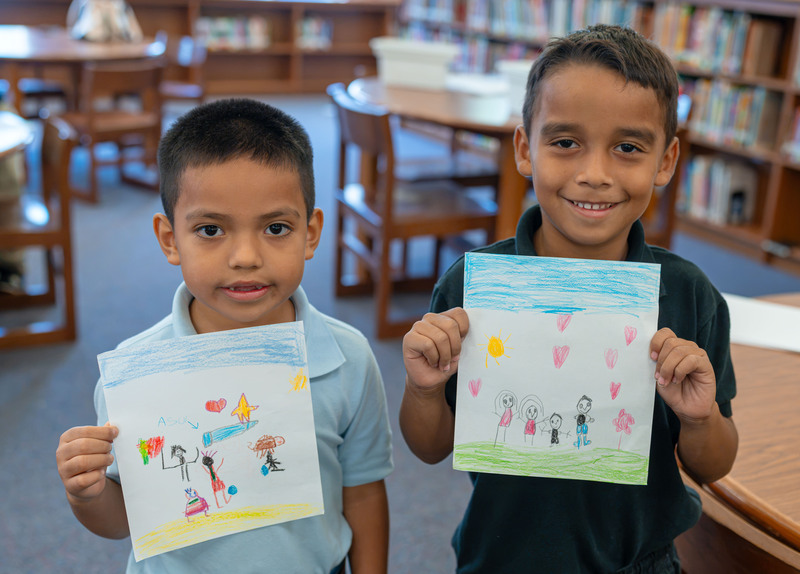 two young boys holding pictures they drew of their families