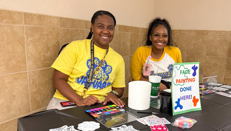two women sitting at a table with paint supplies to paint kids faces