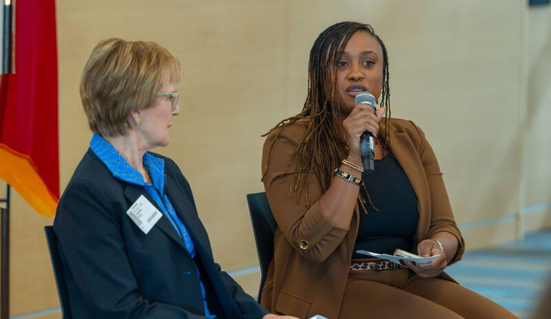 two women sitting in chairs at front of room speaking to high school students