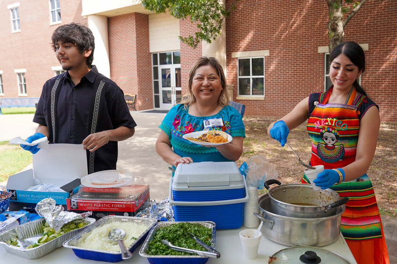 man and two women scoop food onto plates in outside courtyard