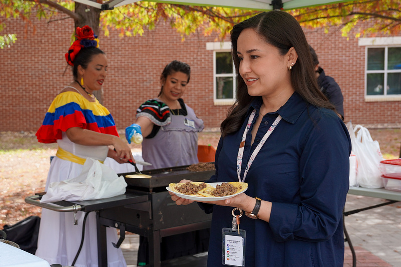woman carrying plate with tacos on it as two women behind her serve food.