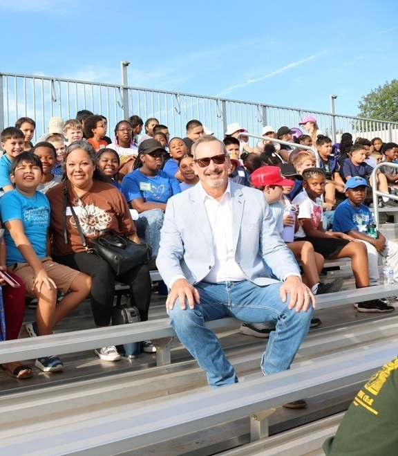 man sitting in front of elementary age students in bleachers
