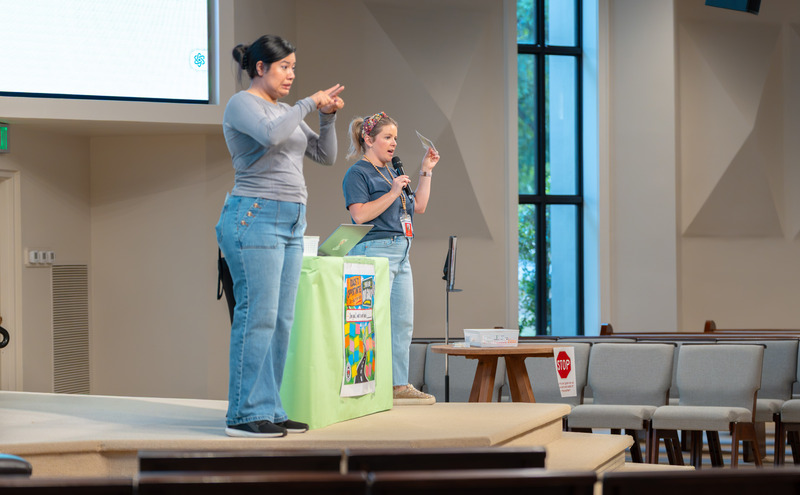 two women on stage talking to crowd, one speaking, one doing sign language