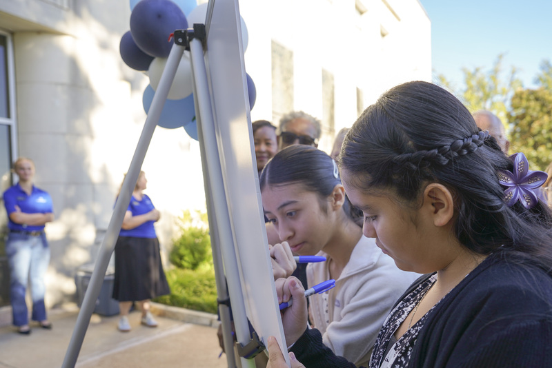 teen girls signing pledgeboard outside a building