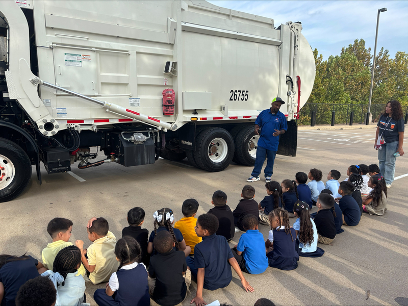 Bonner students sit outside beside a garbage truck while a City of Tyler solid waste worker talks with them about his job.
