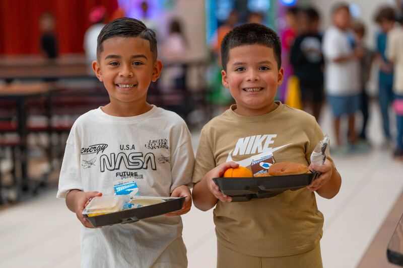 two young boys carrying lunch trays in cafeteria