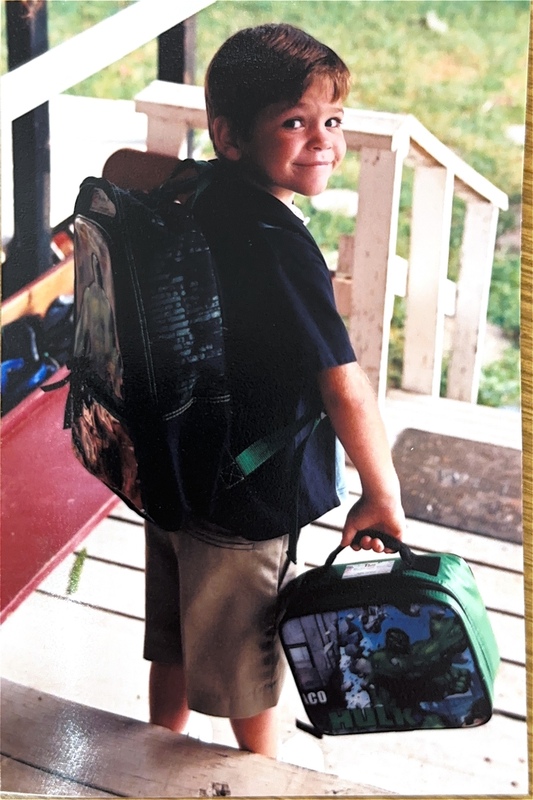 little boy wearing a backpack and carrying a lunchbox walking down steps outside his house