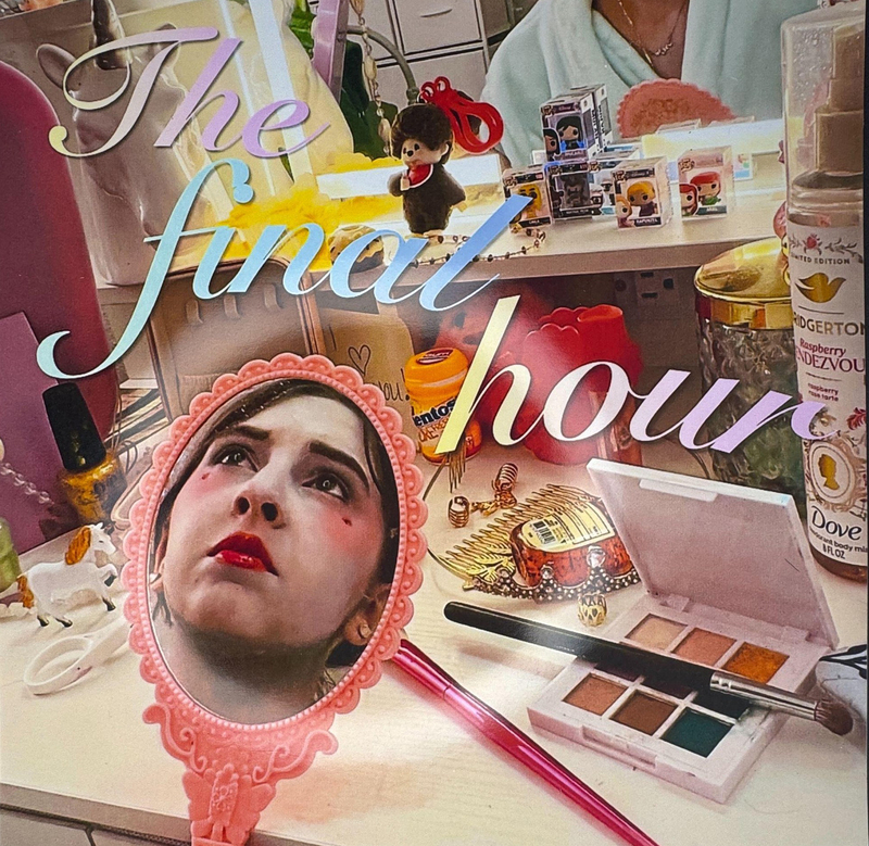 The Final Hour - reflection of girl in hand mirror with makeup on; background of makeup on a table
