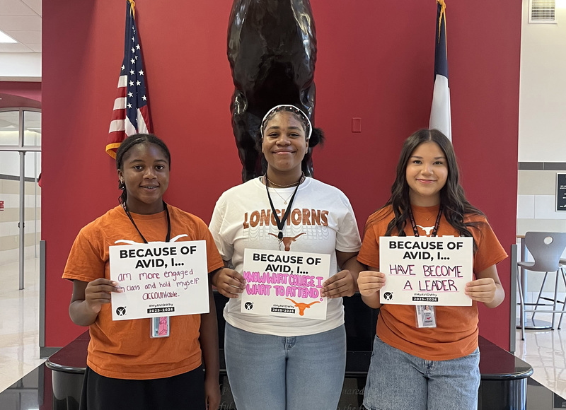three teen girls holding signs "Because of AVID, I..."