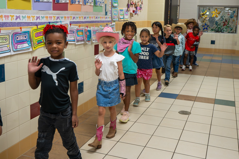 elementary age students waving as they walk in hallway