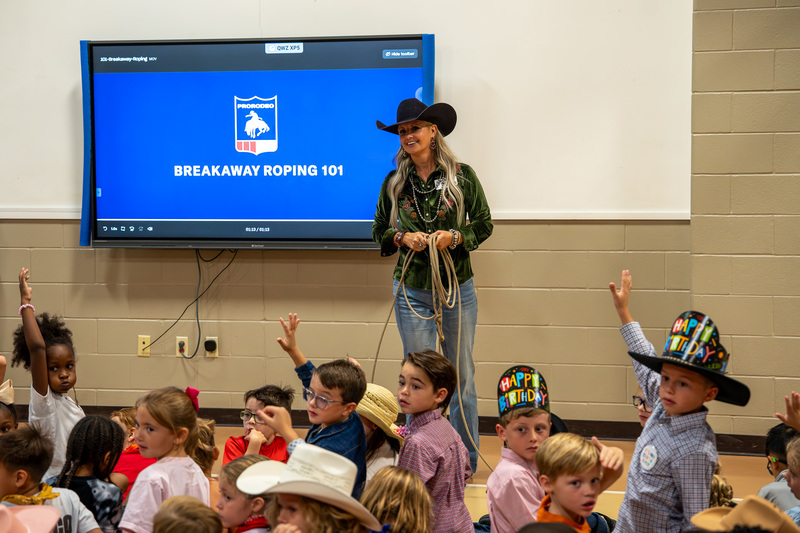 roping cowgirl holding lasso talks to elementary kids