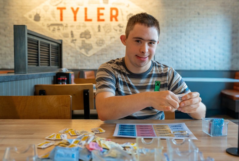 man sitting at table sorting sugar packets by color
