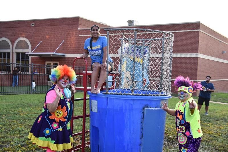 two kids dressed as clowns standing beside a dunking booth with woman inside