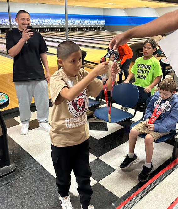 elementary age boy getting handed a medal at bowling alley