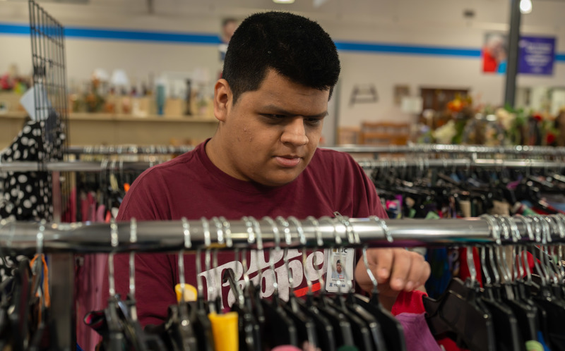 teen boy sorting shirts on rack in store