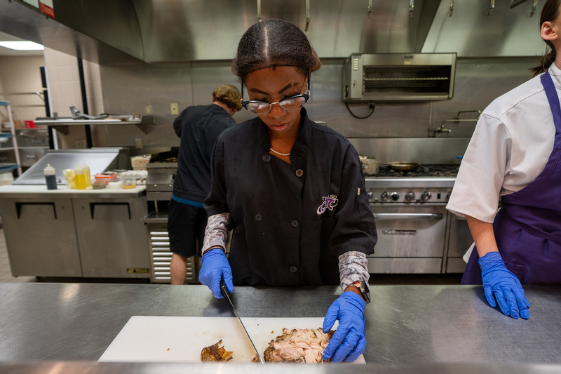 teen girl cutting chicken in kitchen
