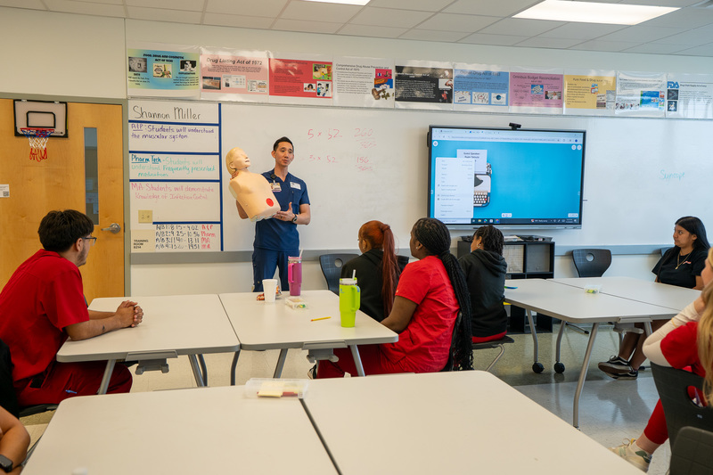 man holding half a mannequin talking to students in classroom