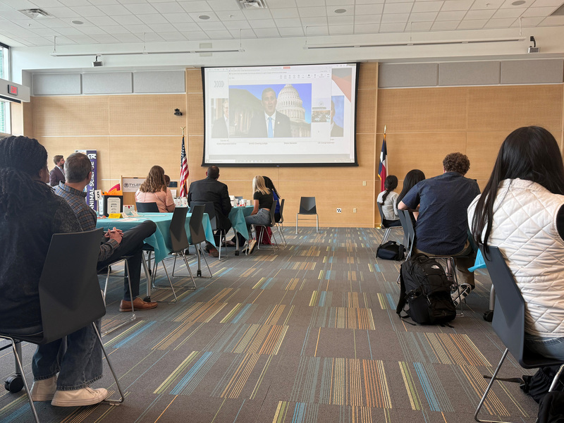 man on big screen talking to crowd of people