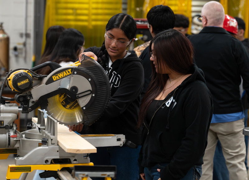 two teen girls working saw in shop class