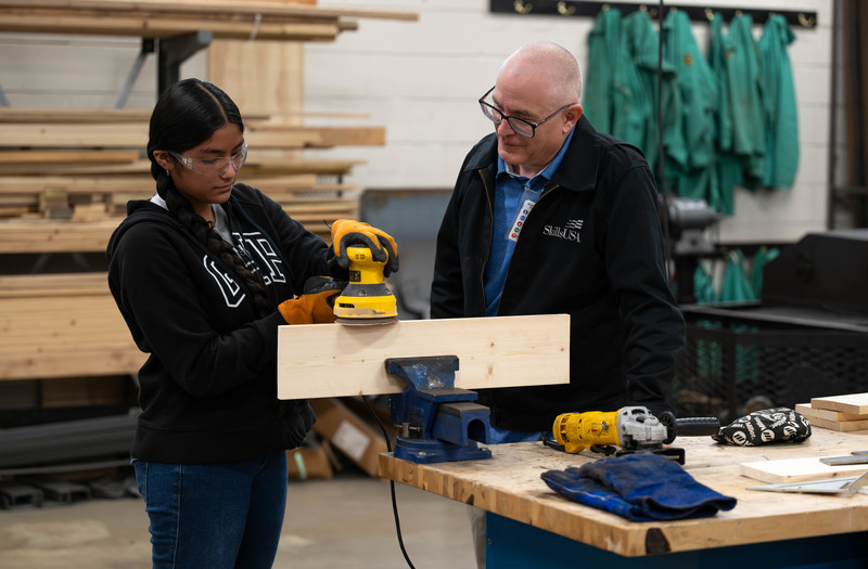 man watching teen girl working with sander in shop class