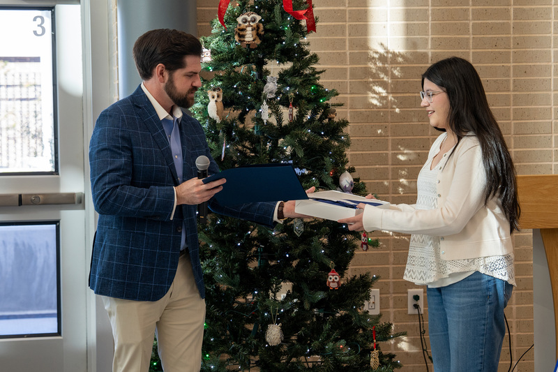 man handing teen girl a box in front of a Christmas tree
