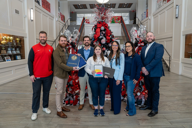 men and women standing in front of Christmas tree in school hallway