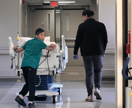 teen boy pushing hospital bed down a hallway