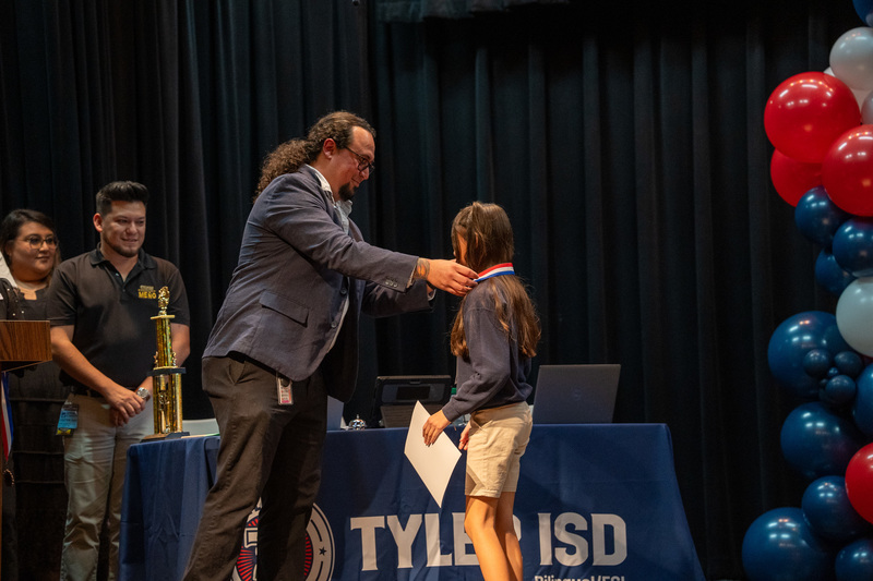 child handed award by an adult on stage