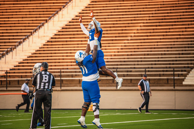 two teen football players, one holding other up in the air