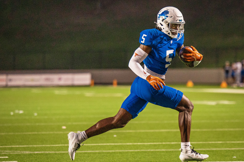 teen boy in blue uniform running the ball on football field