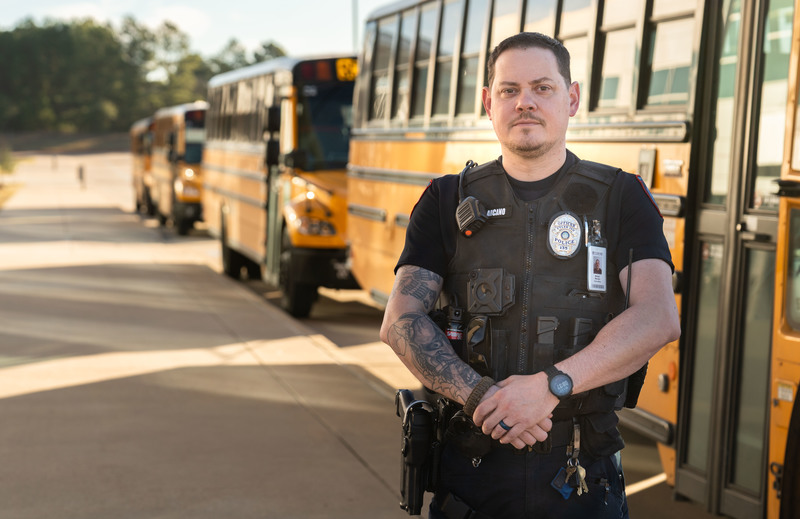 man in police uniform standing beside line of school buses