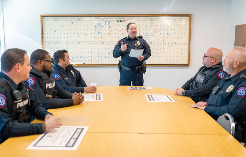 men in police uniforms sitting around a table while another man in uniform talks to them