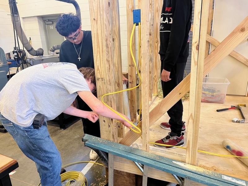 teen boys running wire through frame of house