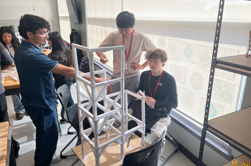 teen boys building roller coaster out of paper