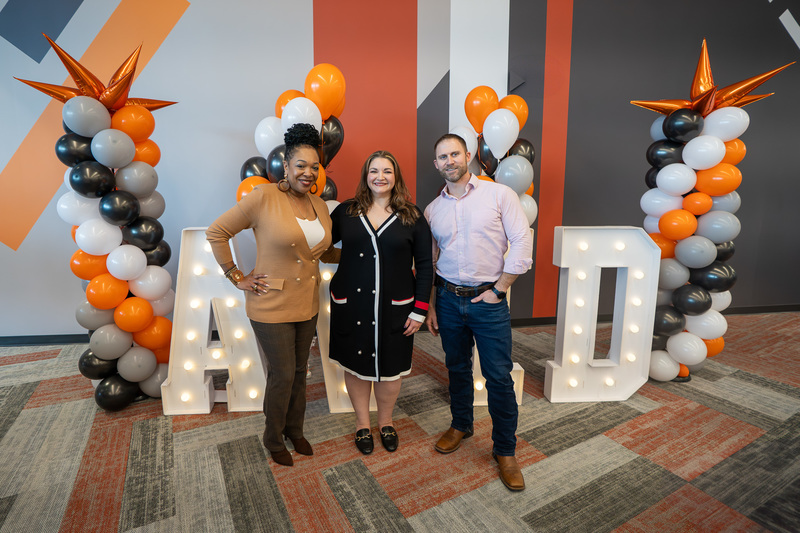 two women and a man standing in front of AVID sign with balloons