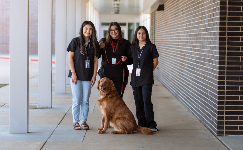 teen girls in black scrubs standing behind dog