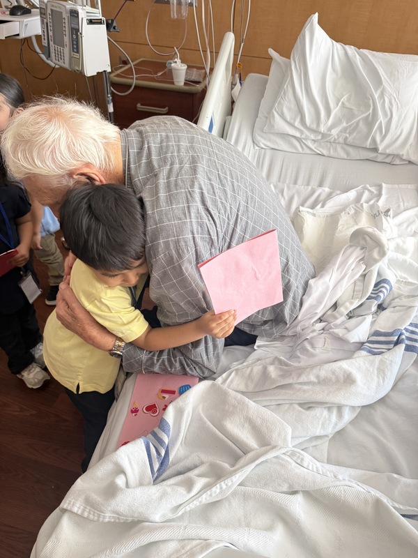 young boy hugging elder gentleman in hospital bed