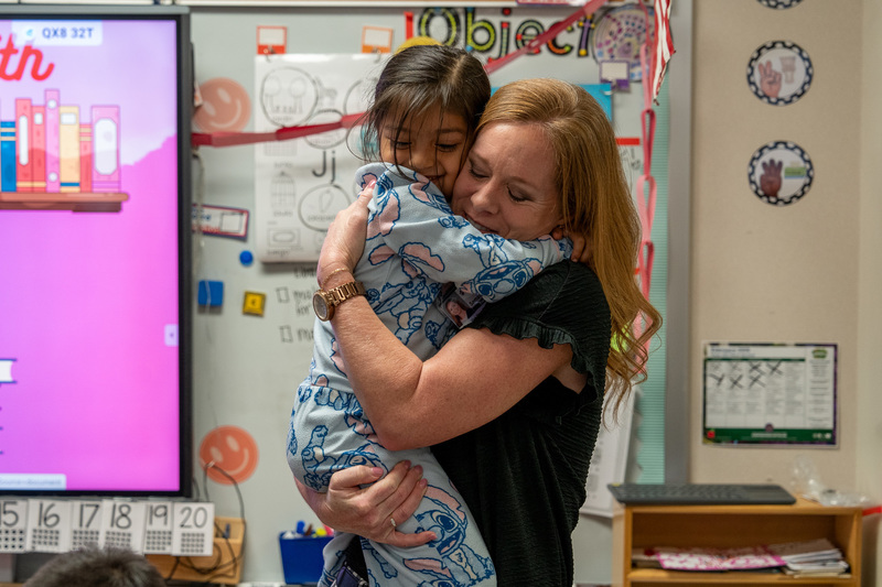 young girl and woman hugging in classroom
